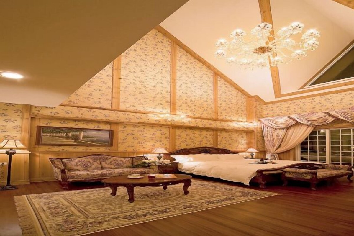 A spacious room with a large bed, a sofa, a coffee table, and a chandelier.