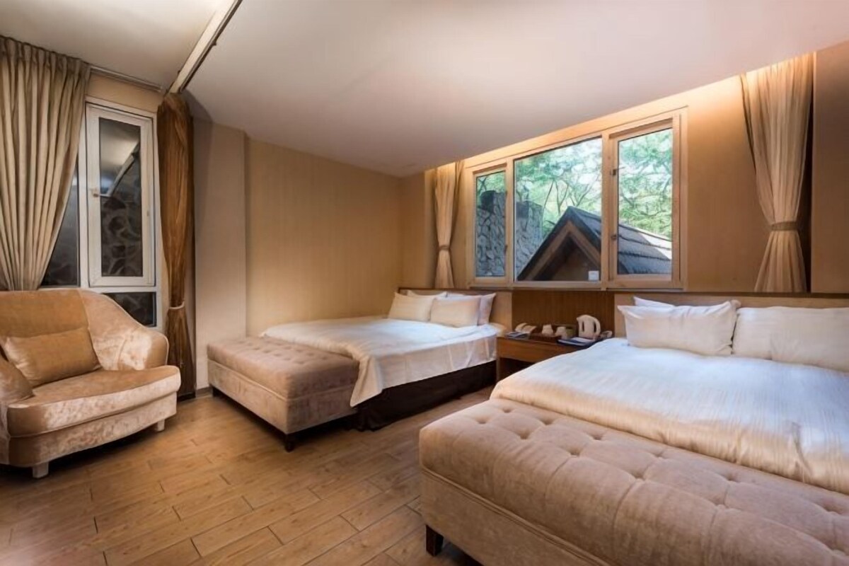 Quarto com duas camas, um sofá, uma janela com cortinas e piso de madeira.