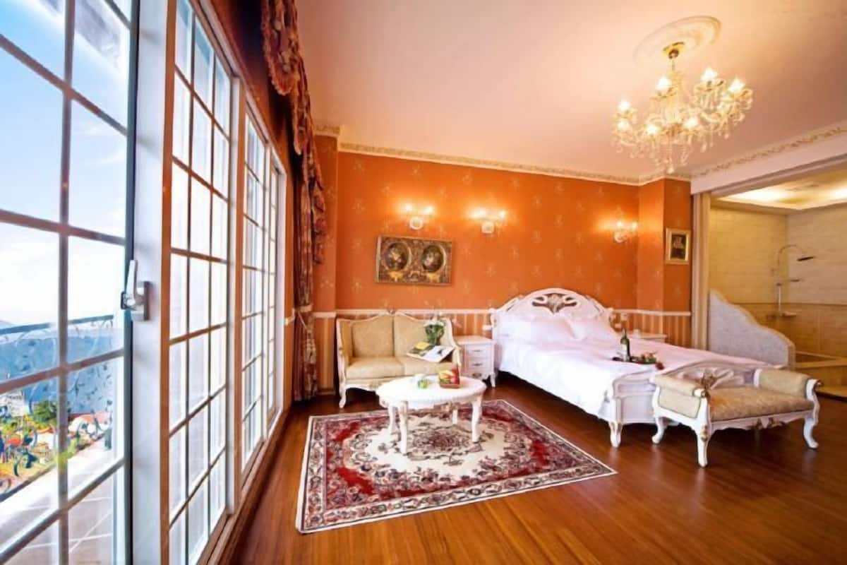 A room with a bed, a sofa, a small table, and a chandelier.