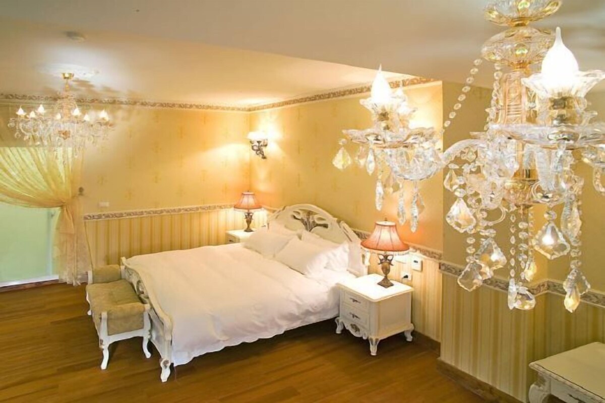 A bedroom with a bed, two bedside tables, a chandelier, and a window with curtains.