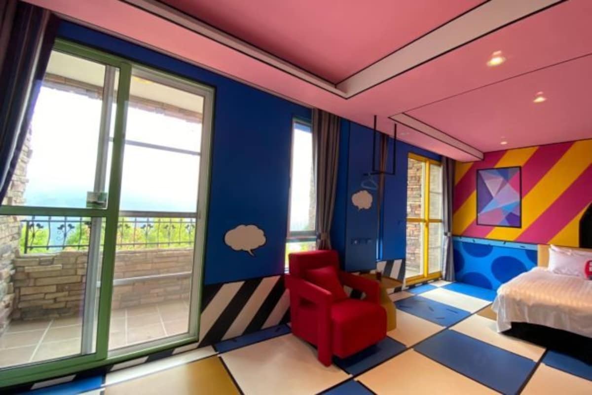 Quarto com uma janela grande, uma cadeira vermelha, uma cama e um design colorido na parede.