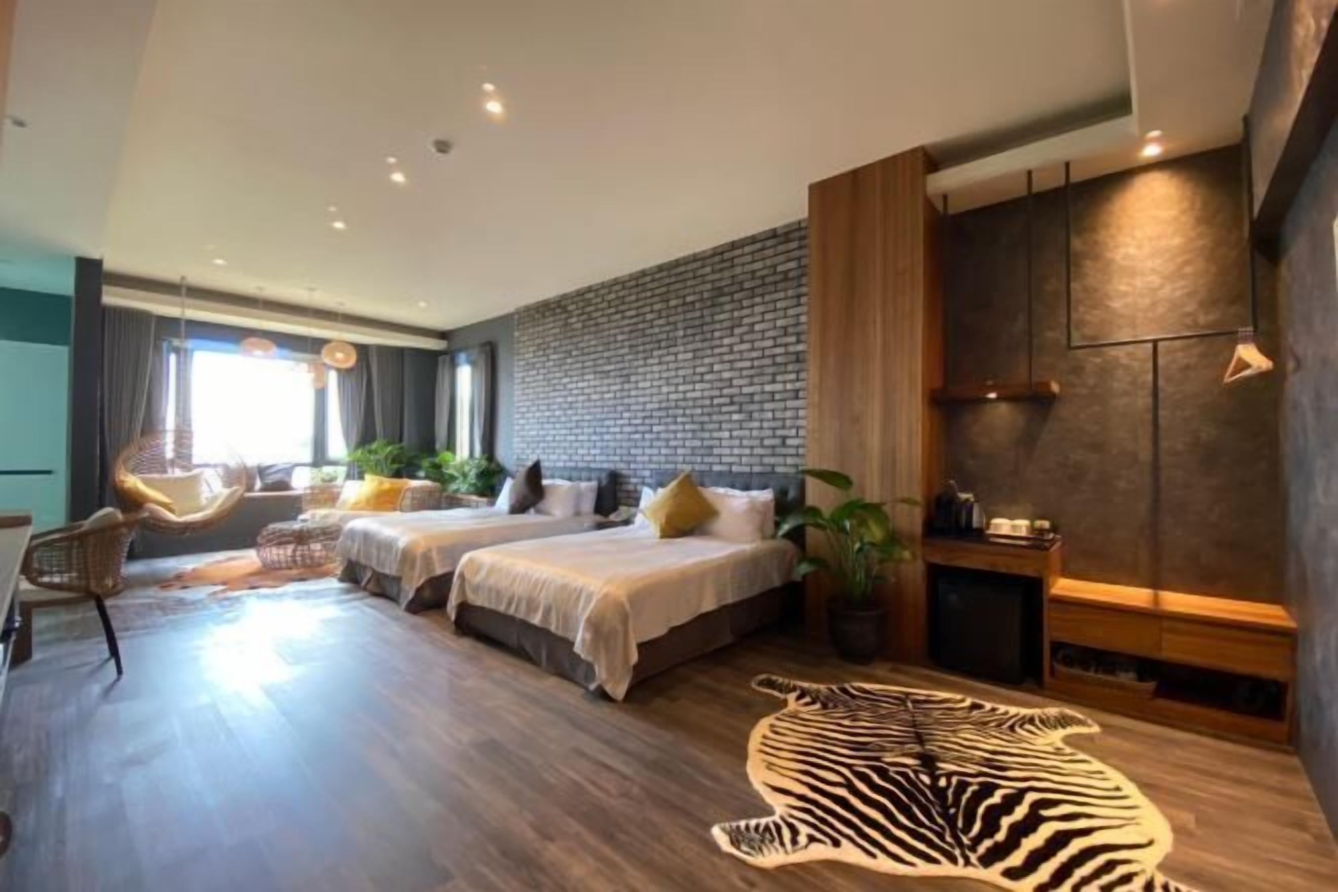 A modern hotel room with two beds, a zebra rug, and a brick wall.