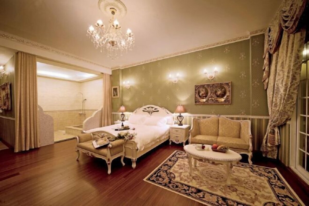 A room with a bed, a sofa, a small table, and a chandelier.