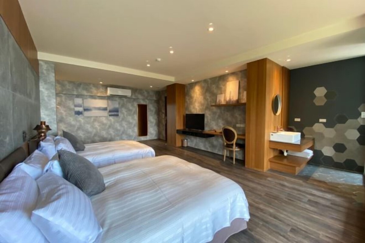 A modern hotel room with two beds, a desk, a TV, and a bathroom.