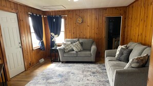 Una sala de estar acogedora con paredes de madera, un sofá gris, un tapete estampado y una puerta con ventana.