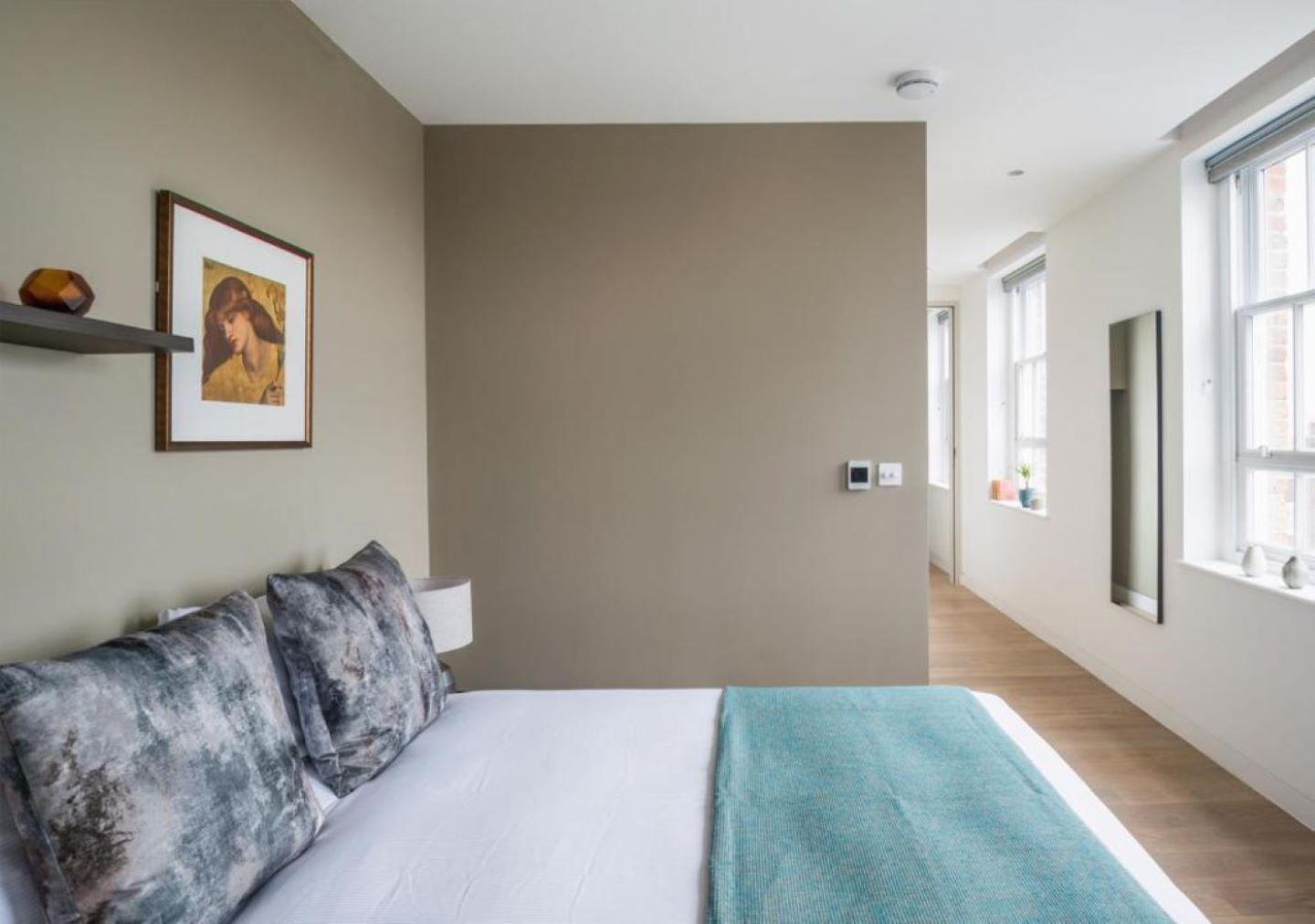 A modern hotel room with a large bed, a framed picture on the wall, and a view of the hallway.