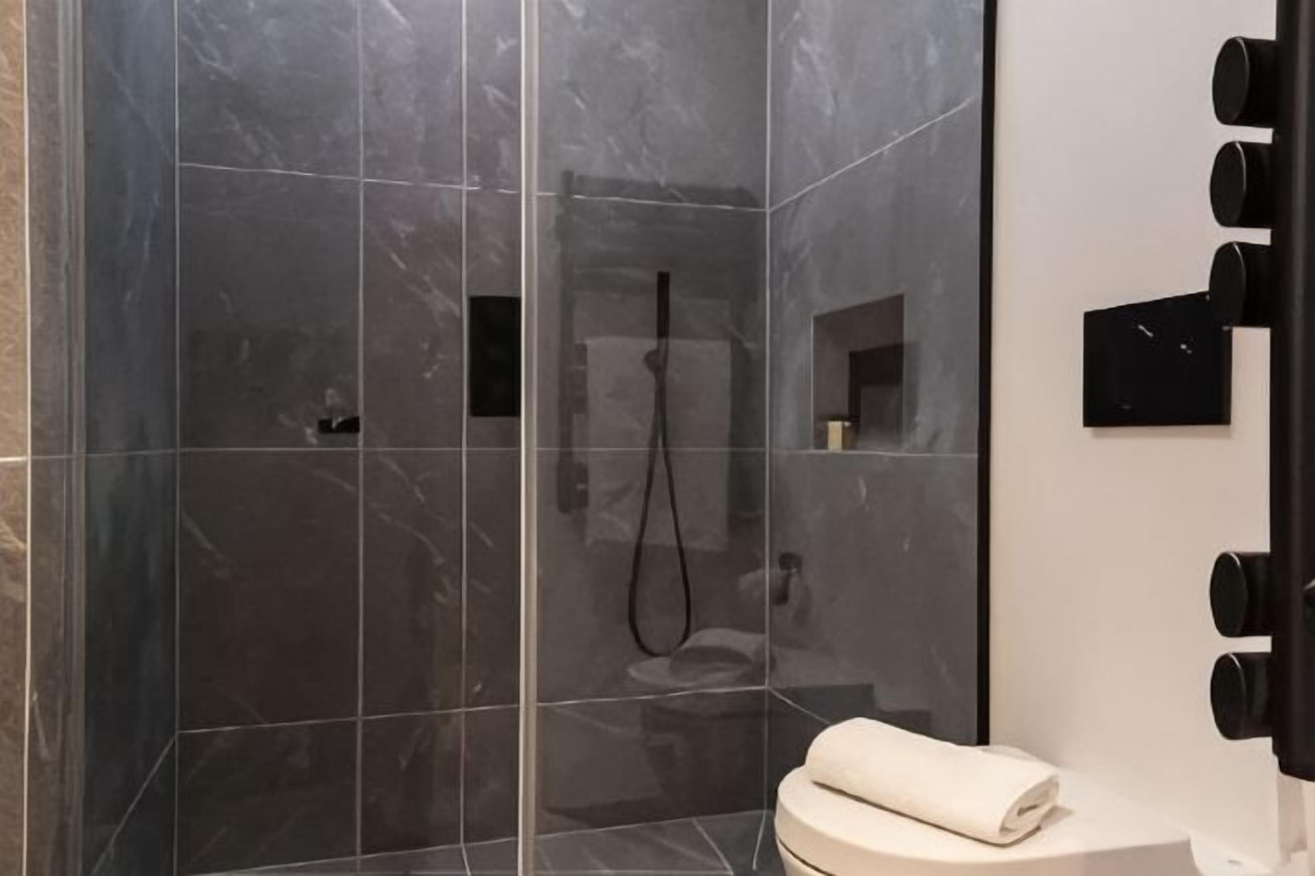 A modern bathroom with a glass-enclosed shower, a toilet, and a mirror with black fixtures.