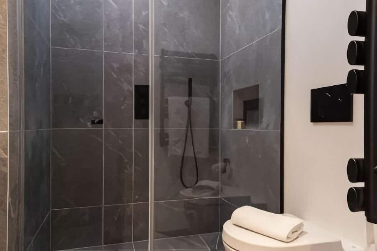 A modern bathroom with a glass-enclosed shower, a toilet, and a mirror with black fixtures.