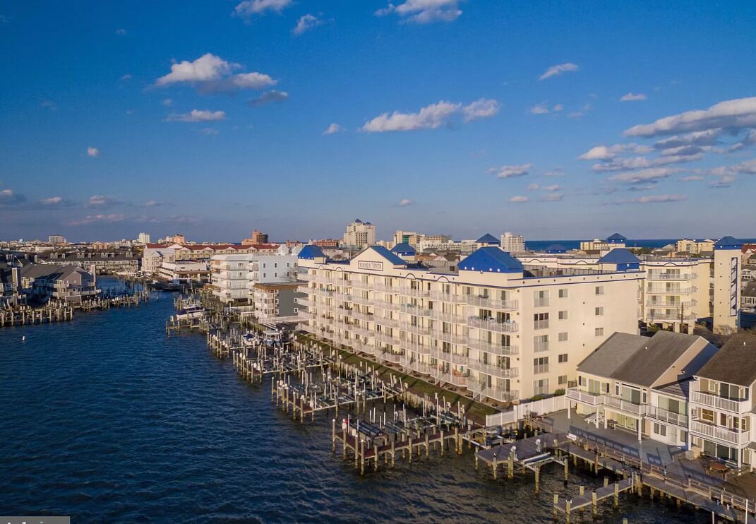 A waterfront hotel with multiple floors, a dock extending into the water, and a clear view of the city skyline in the background.