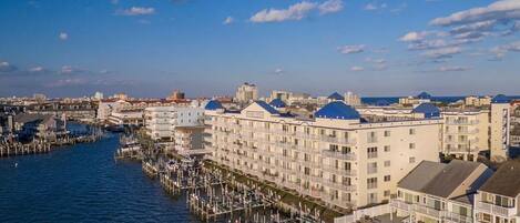 A waterfront hotel with multiple floors, a dock extending into the water, and a clear view of the city skyline in the background.