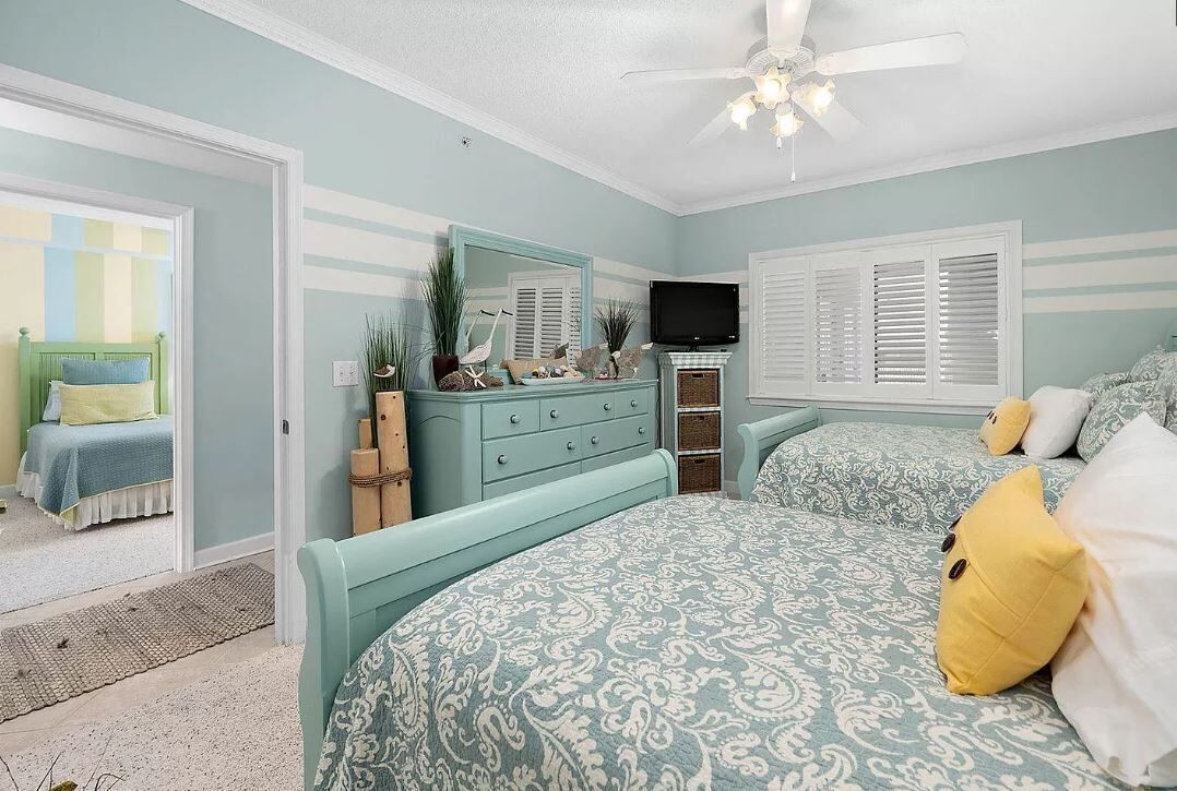 Un dormitorio con cama, cómoda, televisor y ventilador de techo.