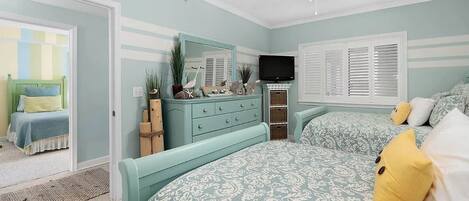 Un dormitorio con cama, cómoda, televisor y ventilador de techo.