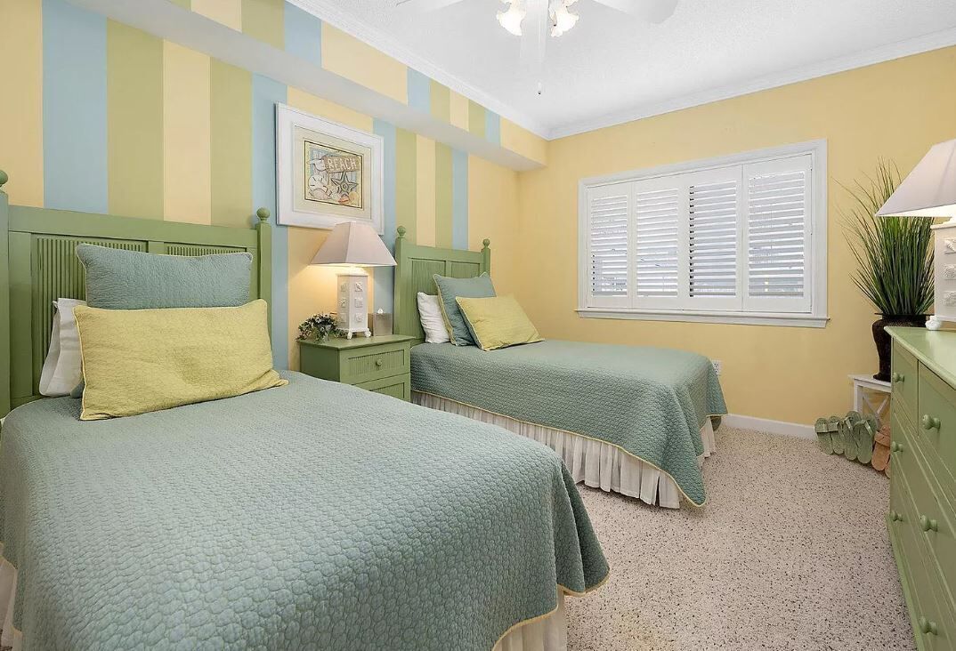 A bedroom with two beds, a nightstand, a dresser, a window with blinds, and a ceiling fan.
