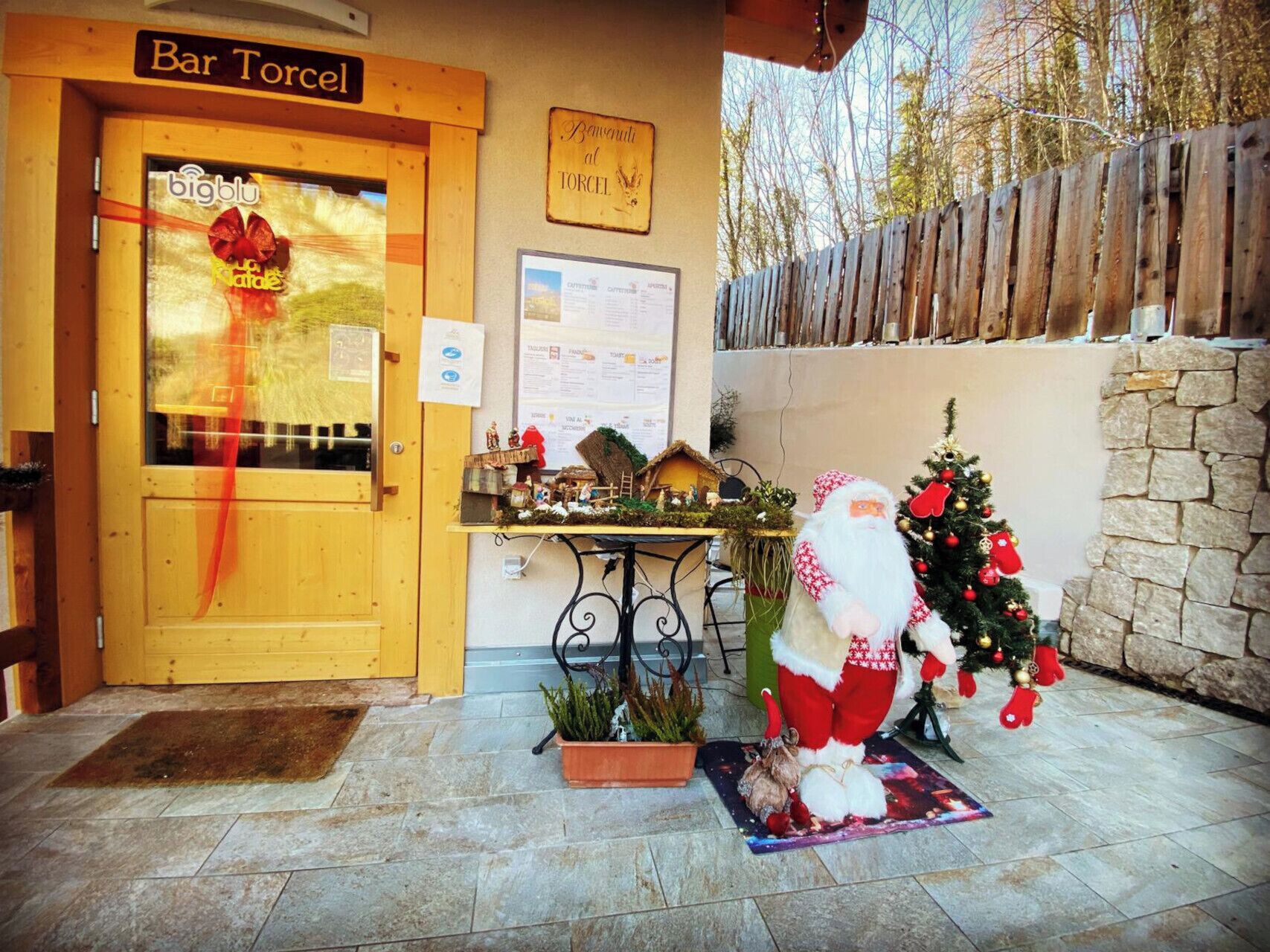 Une porte en bois portant l’inscription « Bar Torcel », décorée pour Noël, avec un petit sapin et une figurine du Père Noël devant.