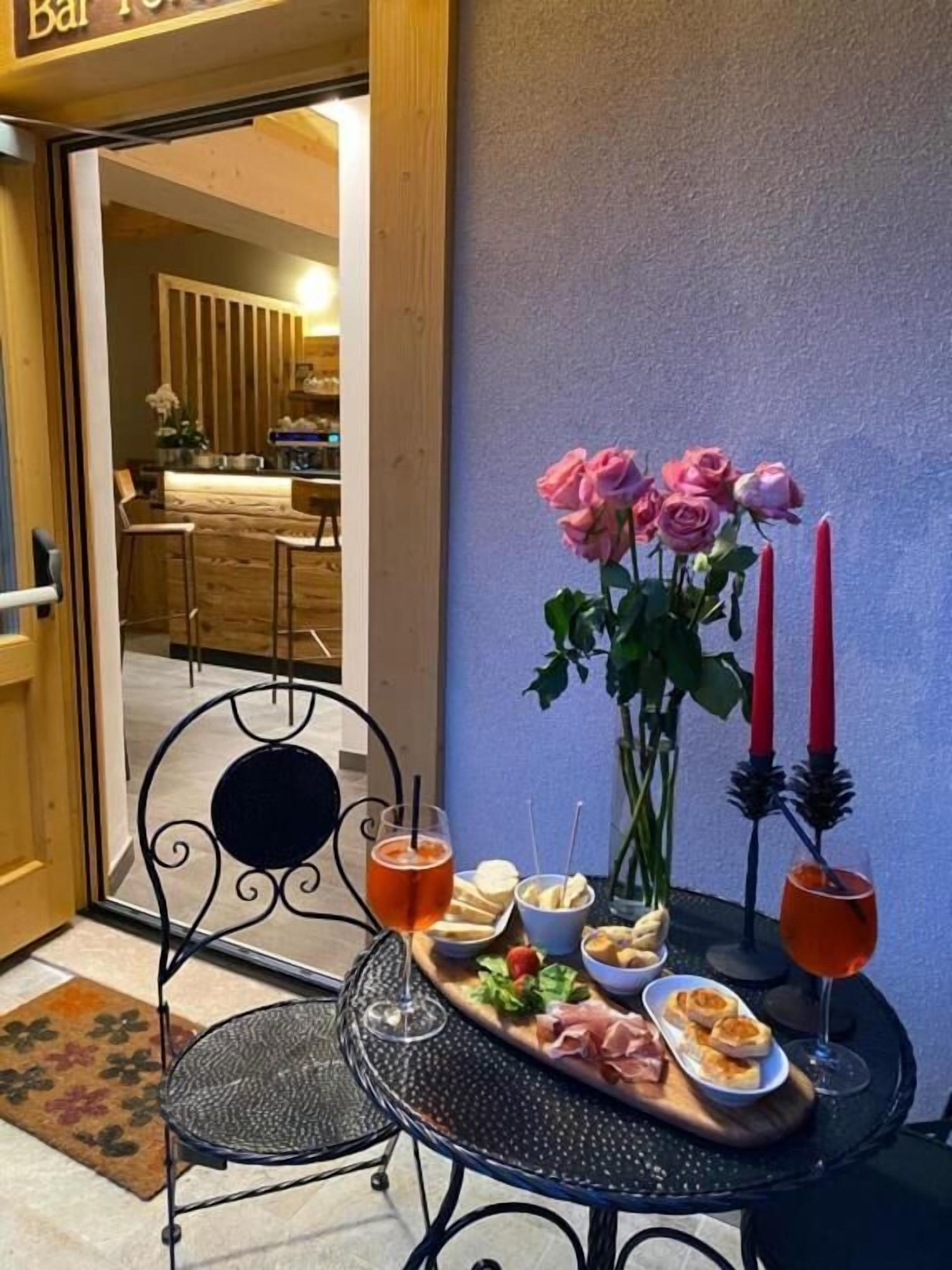 A table with a tray of food, drinks, and a vase of roses outside a bar.