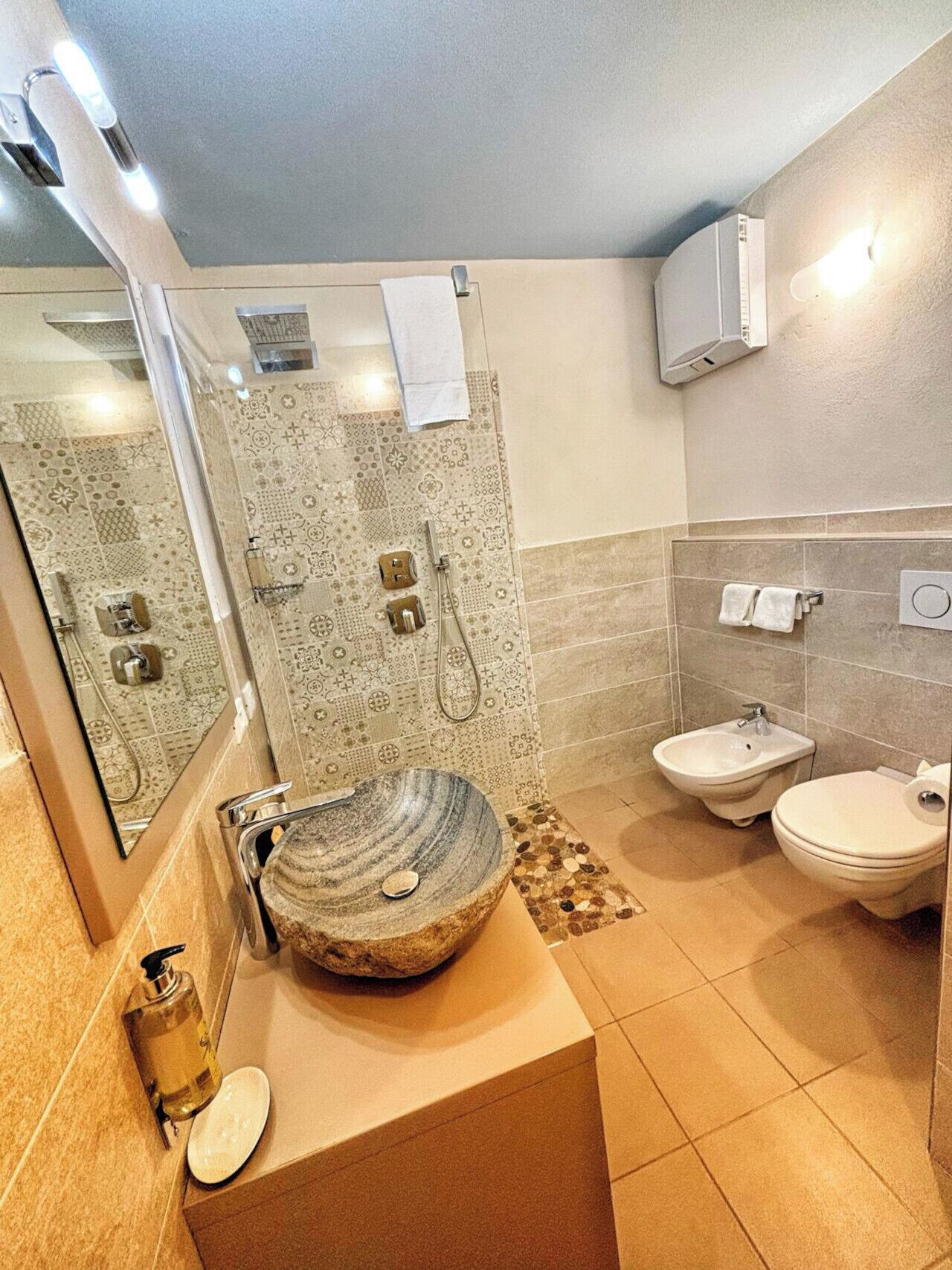 Een badkamer met een stenen wastafel, een toilet, een douche en een bidet.
