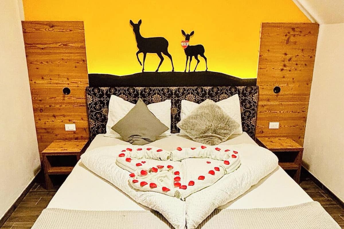 A bed with a heart-shaped arrangement of rose petals, two pillows, and a wall art of deer.