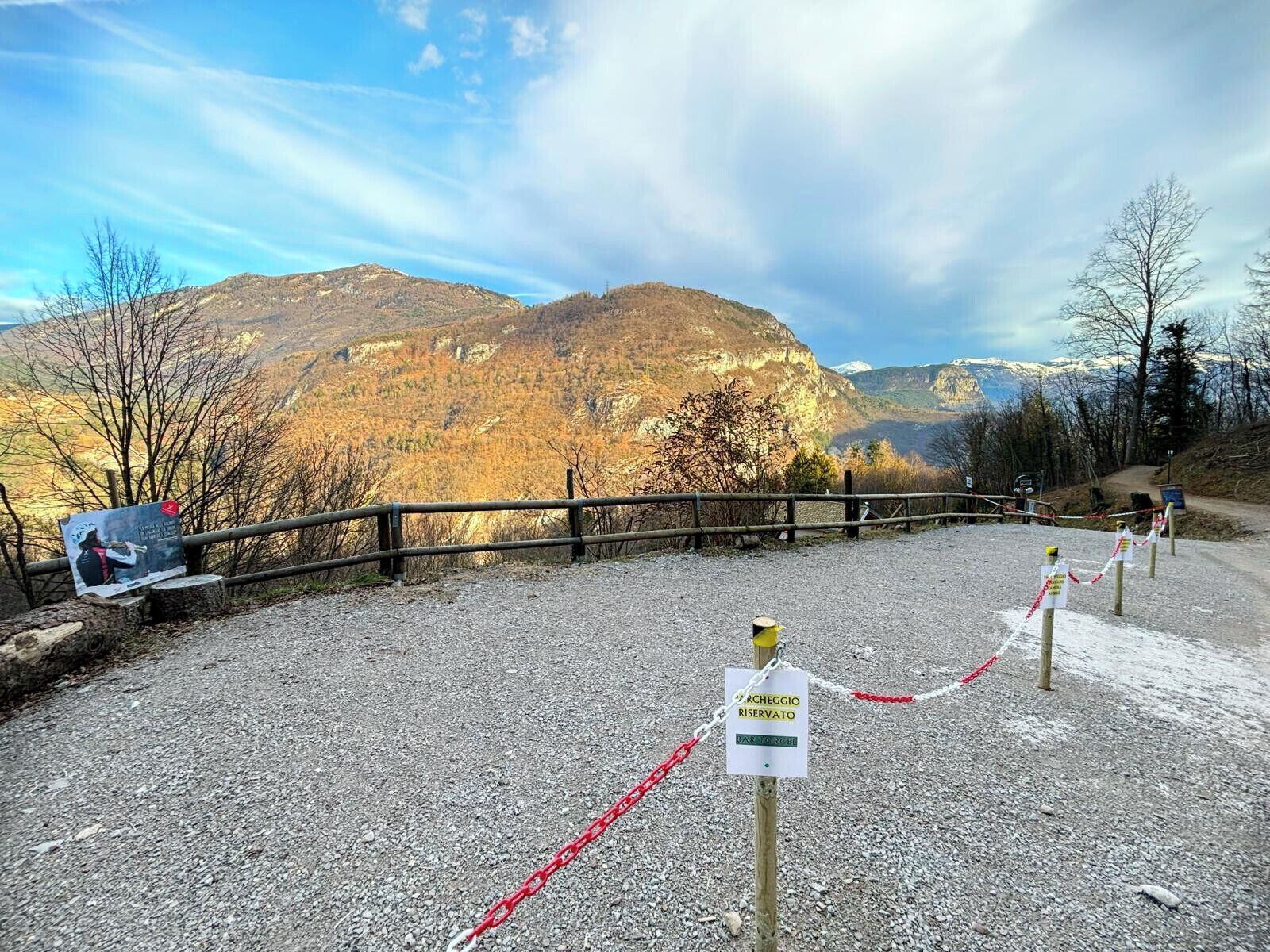 Uma trilha de cascalho leva a uma área montanhosa com uma cerca de madeira e uma placa indicando área reservada.