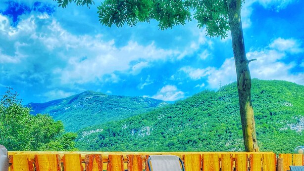 Une piscine avec deux chaises longues, une clôture en bois et une vue sur une colline verdoyante sous un ciel bleu.
