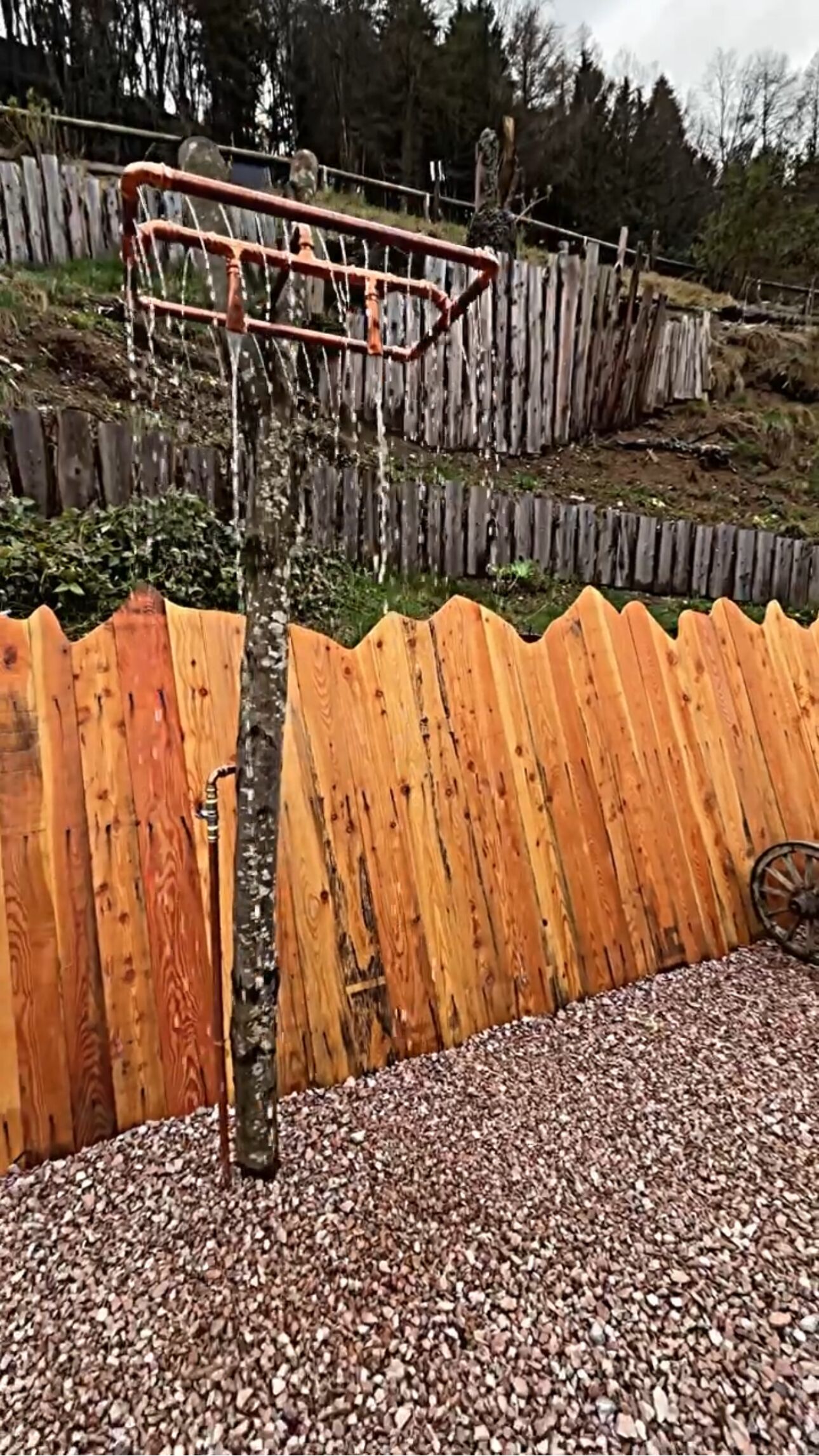 A basketball hoop with a rusty metal structure, a wooden fence, and a gravel ground.