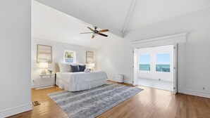 A bedroom with a bed, a ceiling fan, a large window, and a door leading to a balcony. - Beachfront, Large Deck, Sleeps 9, Open, Airy & Spacious (Saint Helena Island)