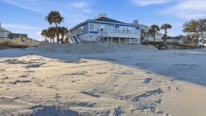 A beachfront house with a balcony, surrounded by sand and palm trees. - Beachfront, Large Deck, Sleeps 9, Open, Airy & Spacious (Saint Helena Island)