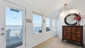 A hallway with a view to a balcony, a wooden cabinet, and a large mirror. - Beachfront, Large Deck, Sleeps 9, Open, Airy & Spacious (Saint Helena Island)