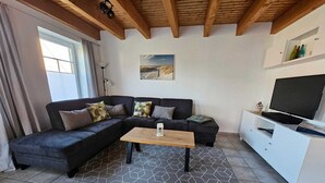 A modern living room with a sectional sofa, a coffee table, a flat-screen TV, and a painting on the wall. - Ferienhaus Meeresbrise in Nessmersiel - NEU in der Vermietung (Dornum)