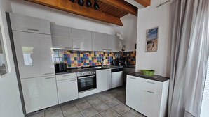 A modern kitchen with white cabinets, a tiled backsplash, and a wooden ceiling. - Ferienhaus Meeresbrise in Nessmersiel - NEU in der Vermietung (Dornum)