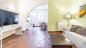 Una sala de estar con televisor, sofá y mesa de centro. En el fondo, hay un comedor con mesa y sillas.