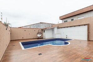 A rooftop swimming pool with a tiled deck, a hanging chair, and a garage door. - Luxuosa Casa com Piscina (Praia Grande)