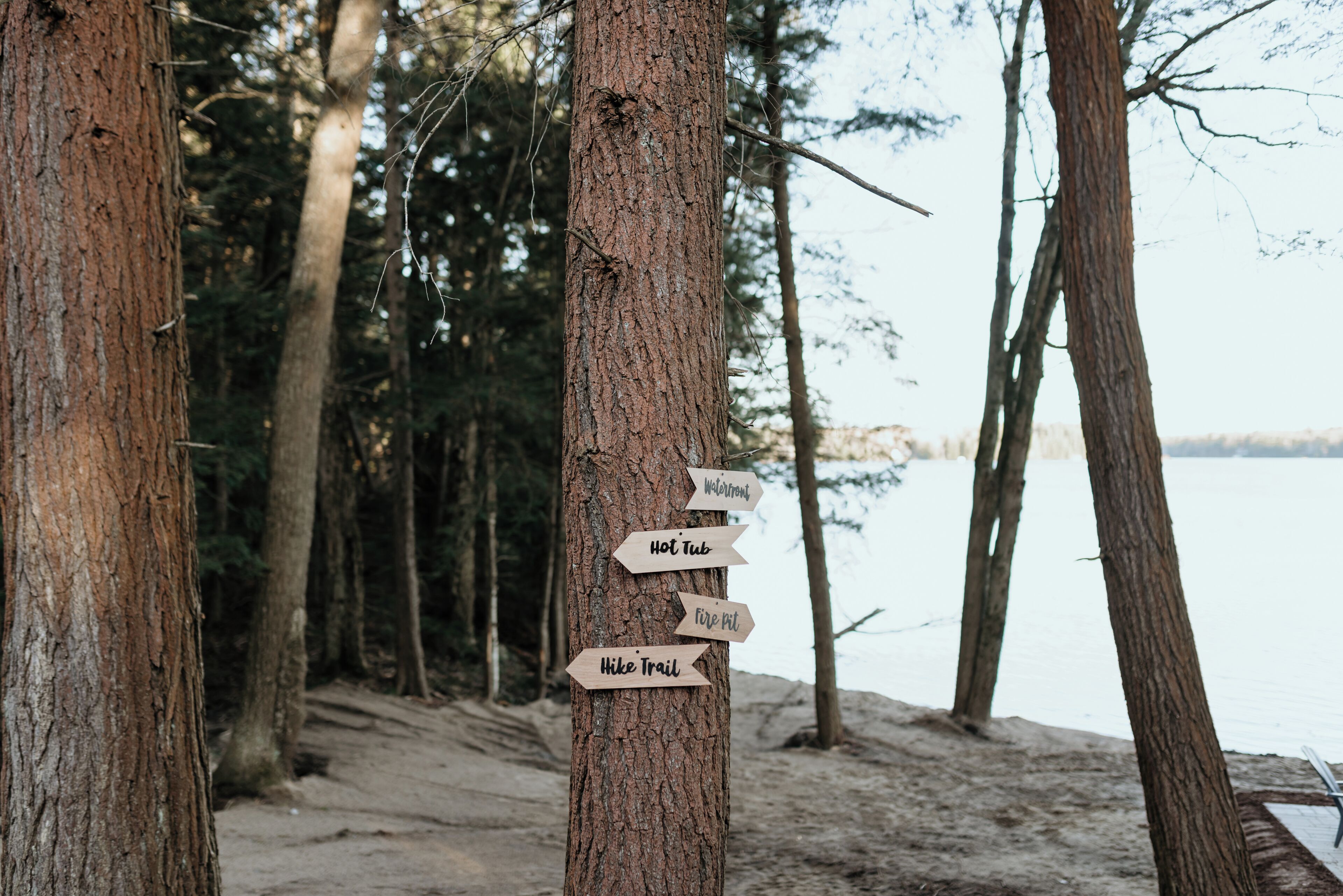 Un segnale di legno con frecce direzionali che indicano 'Welcoming', 'Hot Tub', 'Fire Pit' e 'Hike Trail'.