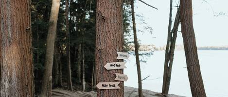 Un segnale di legno con frecce direzionali che indicano 'Welcoming', 'Hot Tub', 'Fire Pit' e 'Hike Trail'.