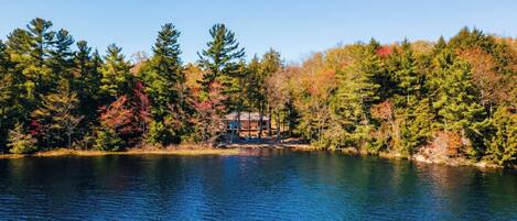 Une cabane au bord d’un lac, entourée d’arbres aux feuilles d’automne.