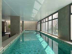 Ein Innenpool mit großen Glaswänden und Fenstern, einem gefliesten Boden und einer Sitzgelegenheit.