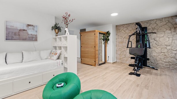 A modern living room with a white sofa, green bean bag chairs, a wooden wardrobe, a stone wall, and a home gym. - Villa Tria Quercus (Vodice)