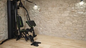 A home gym with a stationary bike and a weight bench against a stone wall. - Villa Tria Quercus (Vodice)