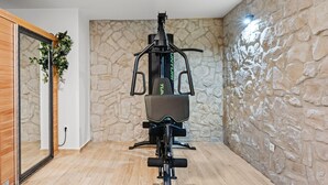 A home gym with a stationary bike, a mirror, and a stone wall. - Villa Tria Quercus (Vodice)
