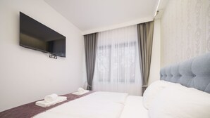 A hotel room with a large bed, a flat-screen TV mounted on the wall, and a window with sheer curtains. - Villa Tria Quercus (Vodice)