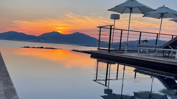 A serene poolside area with lounge chairs and umbrellas, reflecting a sunset over a calm body of water and distant mountains. - Villa Clémentines Porticcio (Grosseto-Prugna)