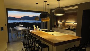 A modern kitchen with a wooden island, bar stools, pendant lighting, and a view of the mountains. - Villa Clémentines Porticcio (Grosseto-Prugna)