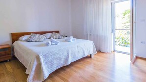 A bedroom with a large bed, wooden headboard, and a sliding glass door leading to a balcony. - Holiday flat with air conditioning (Pula)