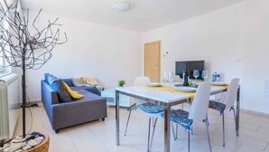 A modern living room with a sofa, dining table, and chairs. There is a television and a plant on the table. - Holiday flat with air conditioning (Pula)