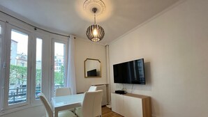 Una sala de estar moderna con comedor, ventanas amplias, un televisor de pantalla plana y una lámpara de techo decorativa.