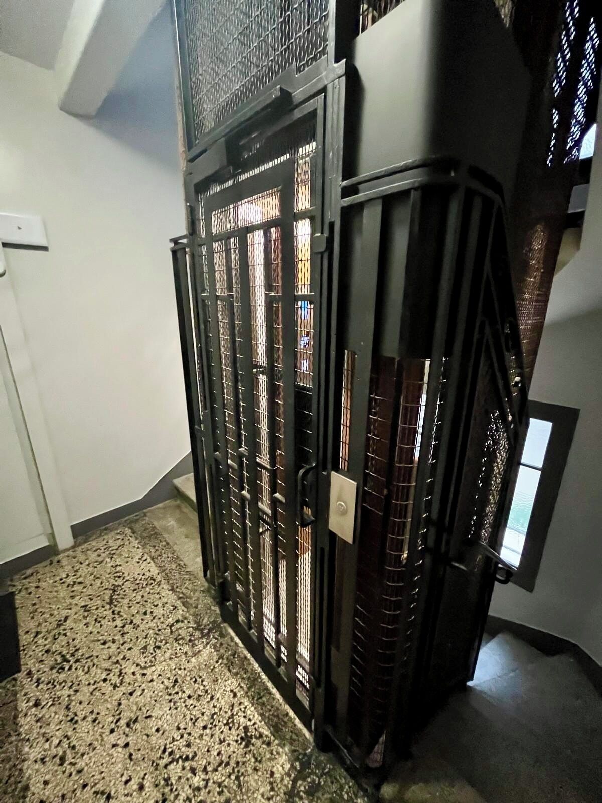A room with a large, dark-colored, metal gate with a lock, a small window, and a textured floor.