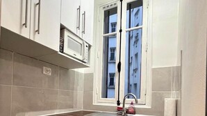 Cocina compacta con armarios blancos, microondas, lavamanos y ventana con vistas a edificios.