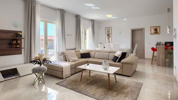 A modern living room with a sectional sofa, a coffee table, and a small stool. There is a fireplace and a dining area visible in the background. - Villa with pool, air conditioning, gym and parking (Vodnjan)