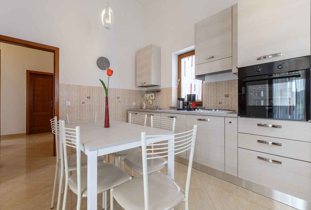 A modern kitchen with white cabinetry, a dining table with chairs, and a built-in oven.