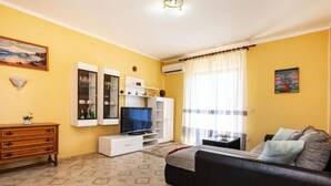 Un salón con sofá, televisor y muebles de almacenaje frente a paredes amarillas.