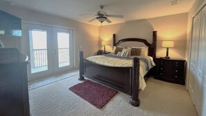 A bedroom with a bed, two bedside tables, a ceiling fan, and a view through a door to a balcony.
